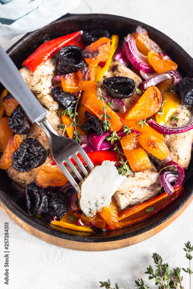Grilled chicken with vegetables (bell pepper, carrot and onion) and dried fruits (apricots and prunes) in a cast-iron pan. Light gray background. Copy space. Healthy food. Grilled chicken with vegetables (bell pepper, carrot and onion) and dried fruits (apricots and prunes) in a cast-iron pan. Light gray background. Copy space. Healthy food.