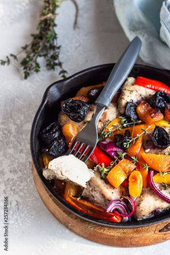 Grilled chicken with vegetables (bell pepper, carrot and onion) and dried fruits (apricots and prunes) in a cast-iron pan. Light gray background. Copy space. Healthy food.