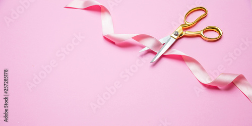 Grand opening. Gold scissors cutting pink satin ribbon, pink background