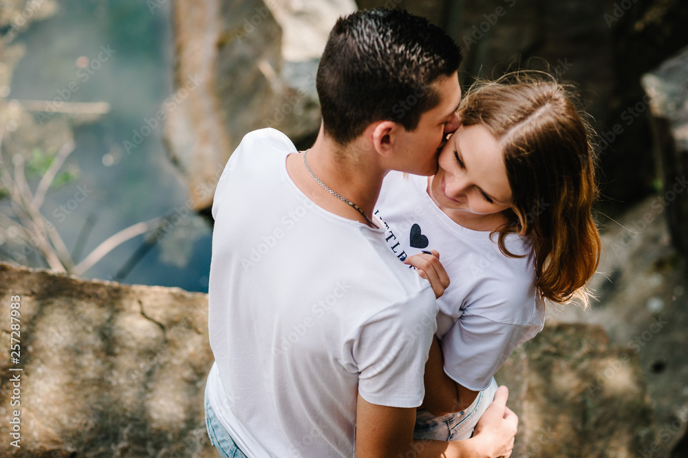 Young couple hugging and kissing on stone near the lake. A man and a woman stand against the background of the rocks. Top view. Nature. upper half. looking at each other. Side view. Close up. Young couple hugging and kissing on stone near the lake. A man and a woman stand against the background of the rocks. Top view. Nature. upper half. looking at each other. Side view. Close up.