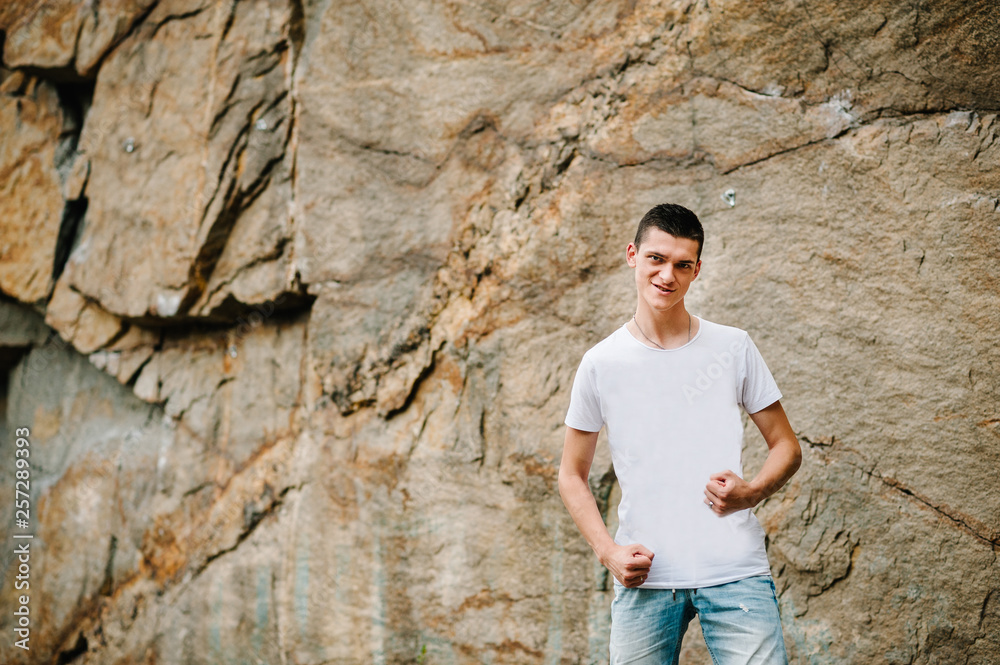Strongman stand on background of the large rocks wall on a big stone. upper half. looking at the camera. Close up. Place for text and design. Man poses at cliff of mountain on nature. Strongman stand on background of the large rocks wall on a big stone. upper half. looking at the camera. Close up. Place for text and design. Man poses at cliff of mountain on nature.