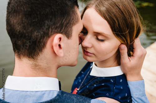 The face of young people. A couple standing, hugging, kissing on the background lake and on a wooden bridge. Close up. headshot, half length. A woman with Make-up her eyes closed.