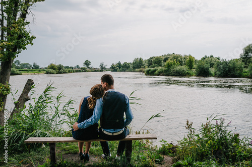 A young couple sitting back on the bench, kissing and hugging near lake. Nature, landscape. View back. Close up.