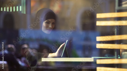 Photography Beautiful Muslim female sitting in cafe, using shopping app on tablet, banking