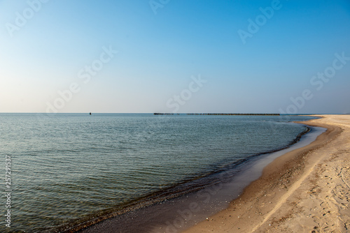 calm sea beach in summer with large rocks and wooden poles from old breakewater in the sea