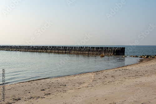 calm sea beach in summer with large rocks and wooden poles from old breakewater in the sea