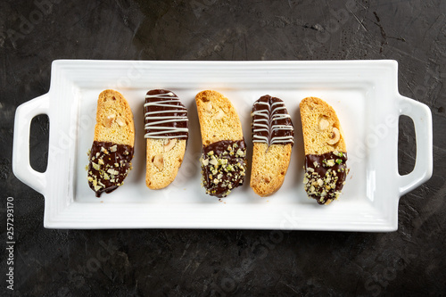 Cantuccini biscuits with chocolate and pistachios on white plate, on stone background. Italian biscotti