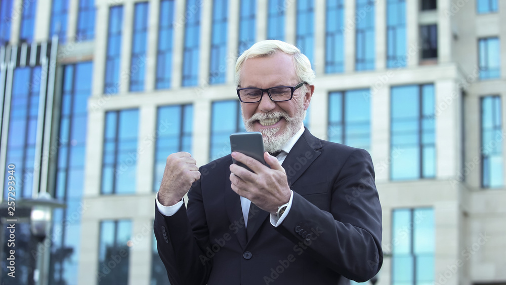 Happy aged businessman receiving good news, making yes-gesture, app for business Happy aged businessman receiving good news, making yes-gesture, app for business