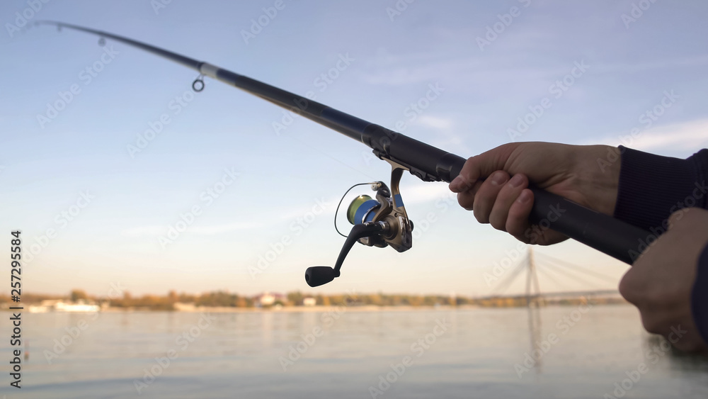 Obraz premium Spinning rod closeup, man fly-fishing near river, active leisure, weekend