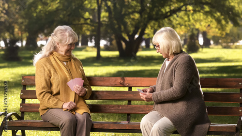 Two old friends playing cards game, sitting on bench in park, golden years