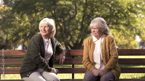 Two grumpy old ladies judging passerby people, sitting on bench in park, pension photo