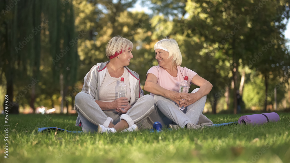 Women chatting sitting on grass after yoga classes on fresh air, healthcare Women chatting sitting on grass after yoga classes on fresh air, healthcare