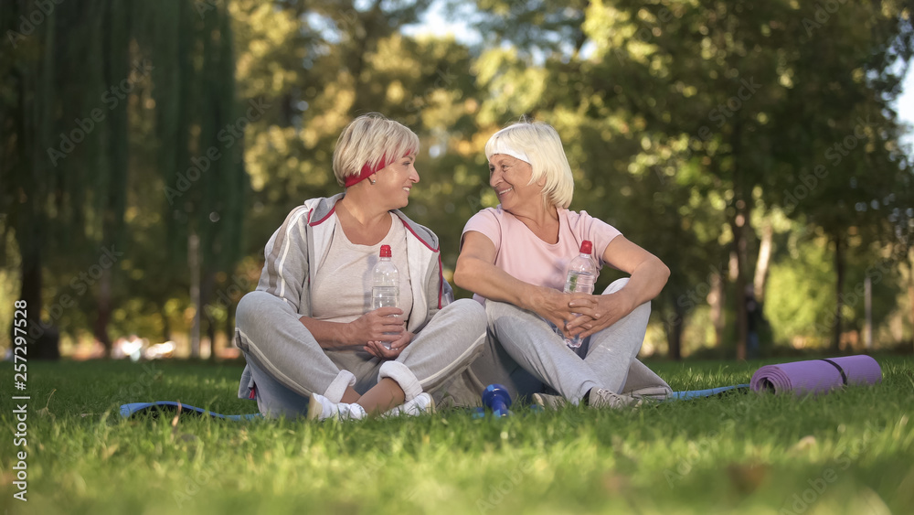 Women chatting sitting on grass after yoga classes on fresh air, healthcare