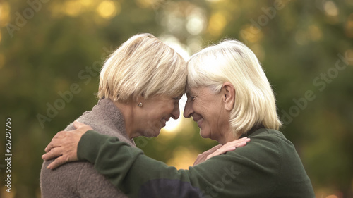 Two mature female friends tightly hugging each other and smiling, happy meeting