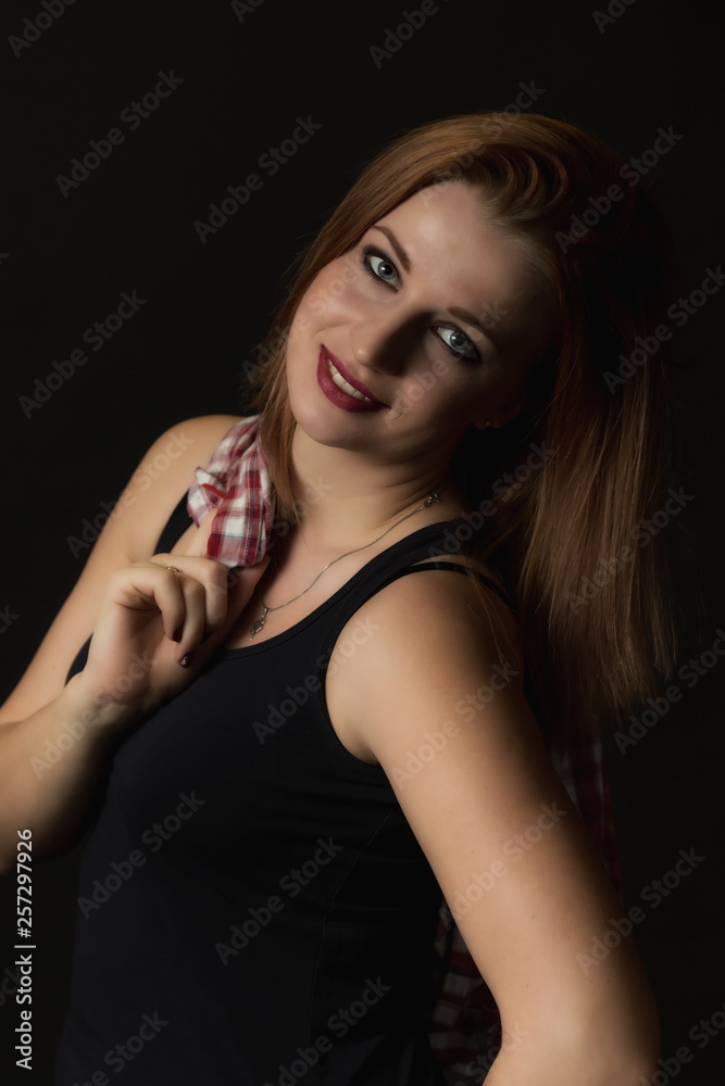 Low key portrait of happy young attractive woman on the black background. Woman is holding a checkered shirt over her right shoulder. Vertically. Low key portrait of happy young attractive woman on the black background. Woman is holding a checkered shirt over her right shoulder. Vertically.