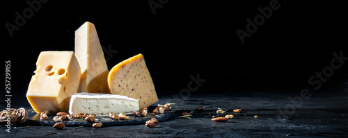 Different kinds of cheese with nuts on dark background, copy space