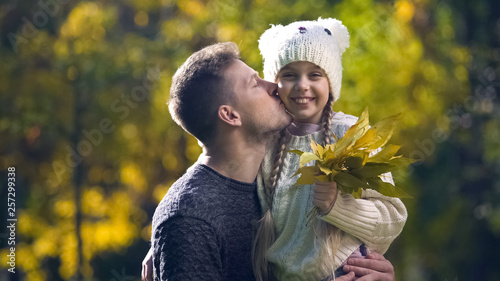 Dad holding daughter in funny hat and kissing  leisure together  autumn stroll