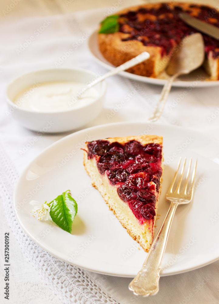 Homemade cherry pie served with cream on a light background with cherry leaves and flowers. Homemade cherry pie served with cream on a light background with cherry leaves and flowers.
