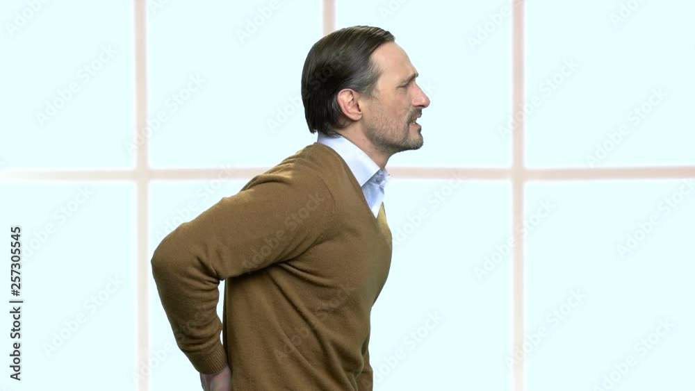 Mature male office worker having back ache. Caucasian male employee having lower back ache, side view. Checkered window background. Mature male office worker having back ache. Caucasian male employee having lower back ache, side view. Checkered window background.