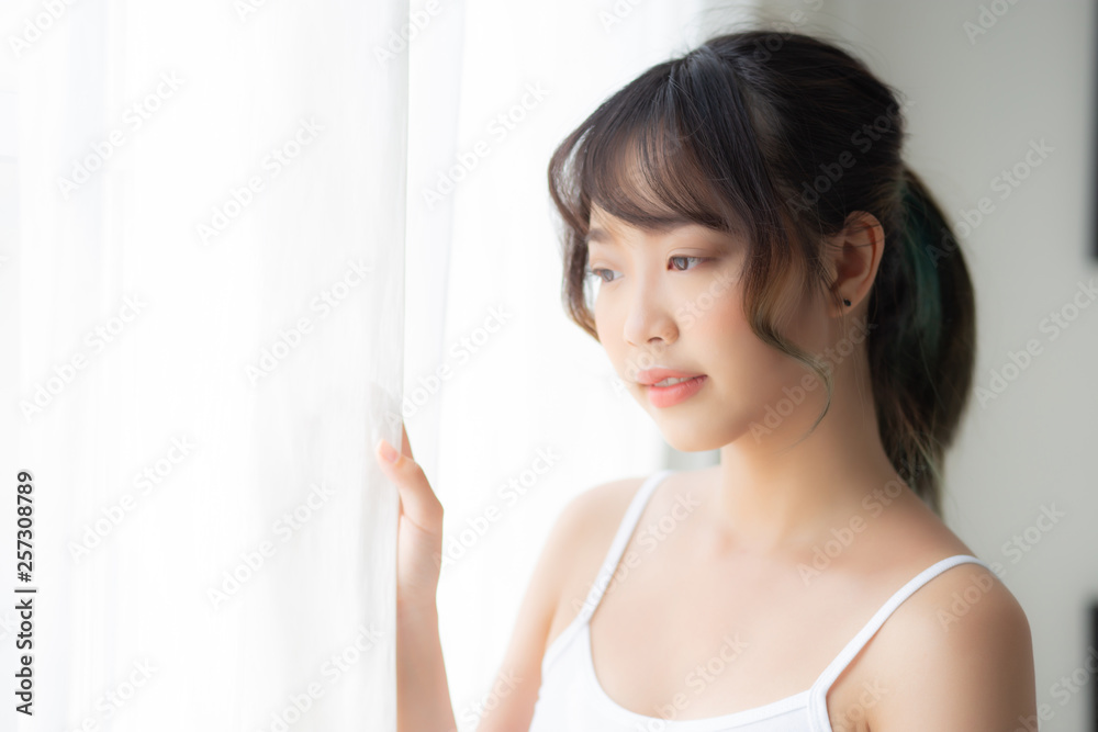 Portrait of beautiful young asian woman standing look at the window and smile while wake up with sunlight at morning, girl happy with fresh and cheerful, lifestyle and relax for wellness concept. Portrait of beautiful young asian woman standing look at the window and smile while wake up with sunlight at morning, girl happy with fresh and cheerful, lifestyle and relax for wellness concept.