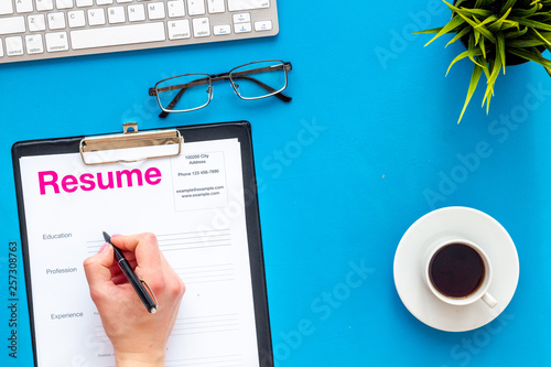 Empoyment concept with resume on blue work desk background with coffee, glasses, keyboard top view photo