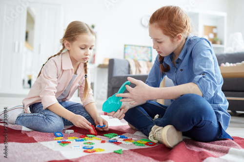 Full length portrait of two sisters playing with puzzles sitting on floor, copy space