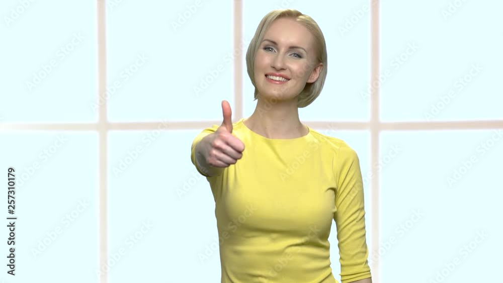 Pretty smiling woman giving thumb up symbol. Happy middle-aged blonde woman with short haircut looking at camera. Checkered window background. Pretty smiling woman giving thumb up symbol. Happy middle-aged blonde woman with short haircut looking at camera. Checkered window background.