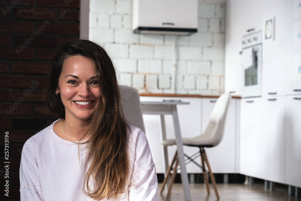 Young smiling woman sitting on the floor in the living room opposite the kitchen Young smiling woman sitting on the floor in the living room opposite the kitchen