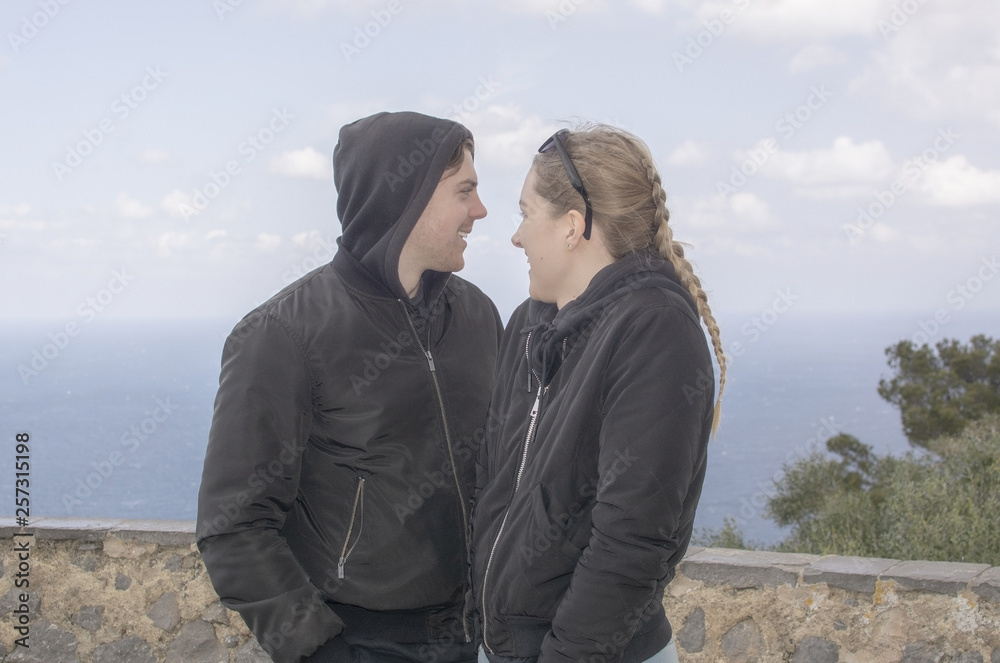 Young beautiful casually dressed couple stand high up watching out to sea Young beautiful casually dressed couple stand high up watching out to sea