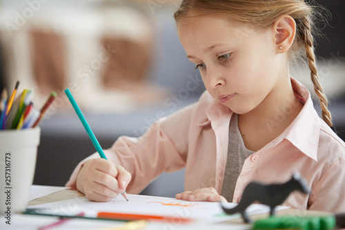 Portrait of cute girl drawing pictures sitting at table home alone, copy space