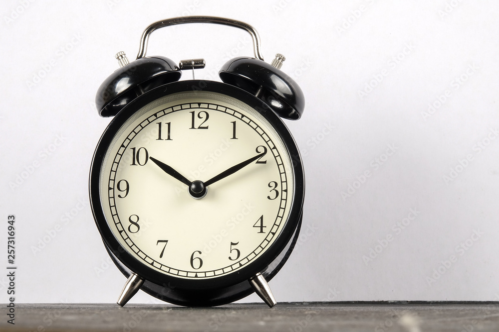 Black alarm clock on the wooden surface against the white background. Black alarm clock on the wooden surface against the white background.