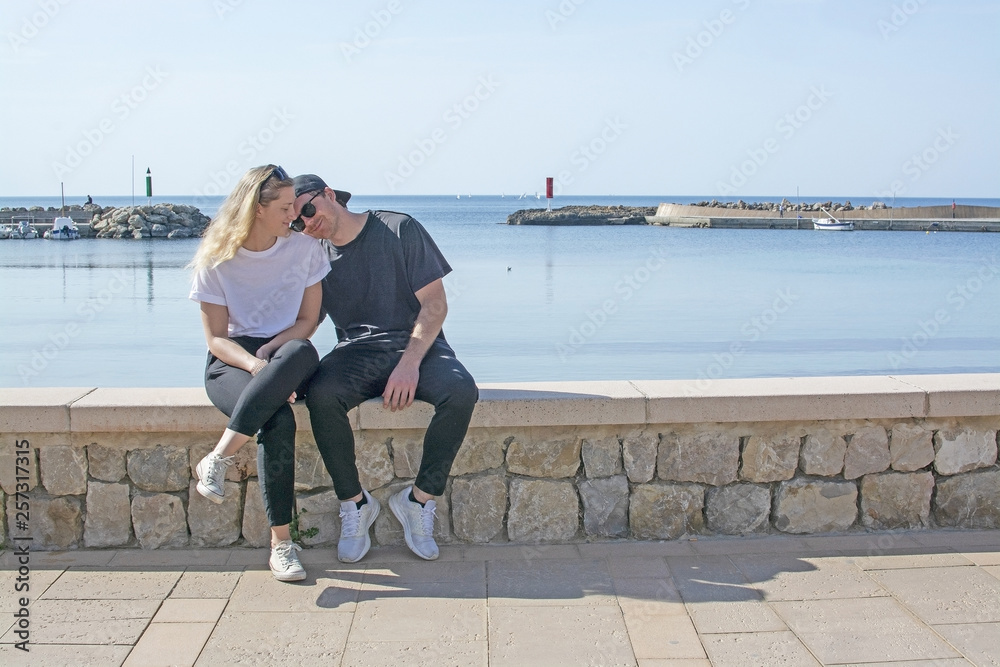 Young natural smiling and casual sporty couple sit on stone wall