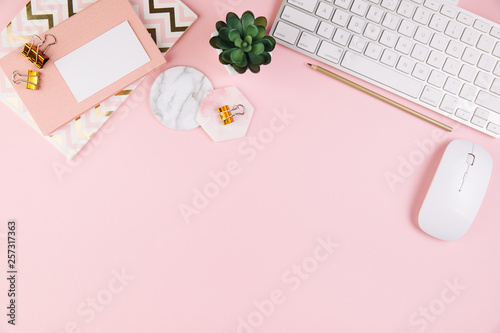 Flat lay, top view pink modern office table desk. Workspace with notebook, clip board, keyboard, office supplies, pencil, green leaf, and coffee cup on white background