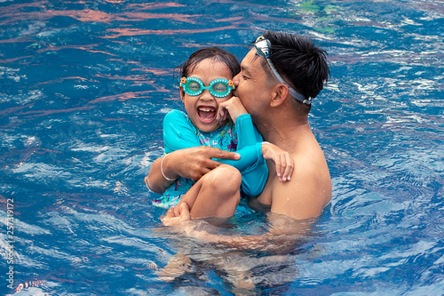 Asian father kissing and playing with his daughter in swimming pool.