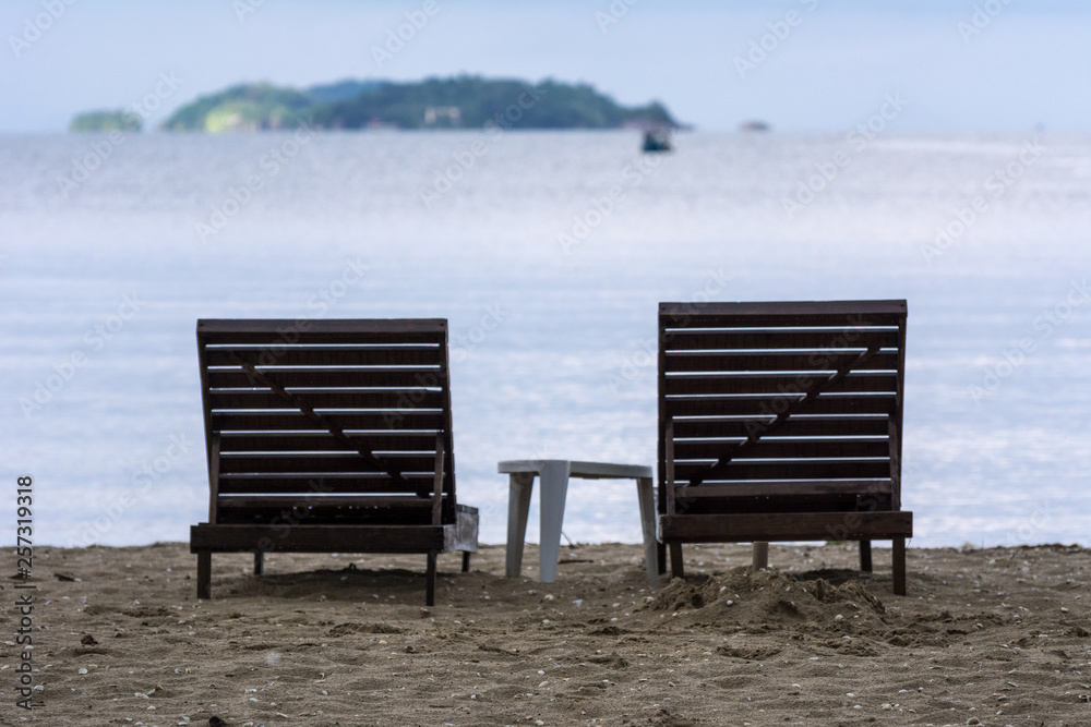 Two wooden beach chairs in front of the sea.