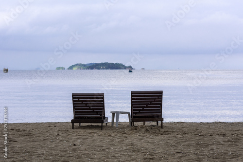 Two wooden beach chairs in front of the sea.