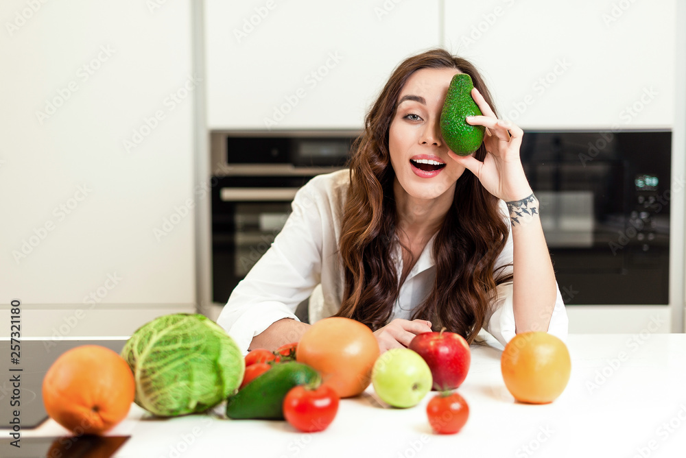Brunette woman on the kitchen with avocado on her eye preparing healthy nutrition salad from fruits and vegetables. Housewife concept Brunette woman on the kitchen with avocado on her eye preparing healthy nutrition salad from fruits and vegetables. Housewife concept