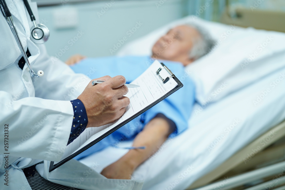 Doctor writing down the diagnosis on clipboard while Asian senior or elderly old lady woman  lying on bed in nursing hospital ward : healthy strong medical concept.  