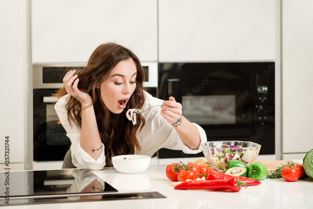 Brunette woman eating homemade soup with pasta and fresh vegetables from a bowl. Housewife concept