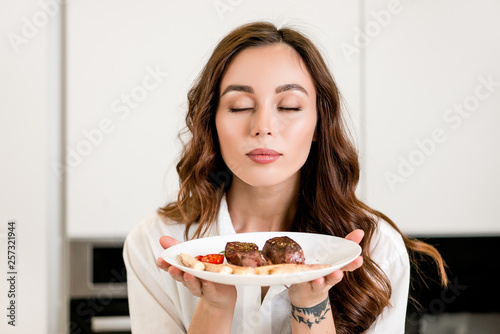 Brunette woman cooking and eating red meat steak with glass of red wine. Housewife concept