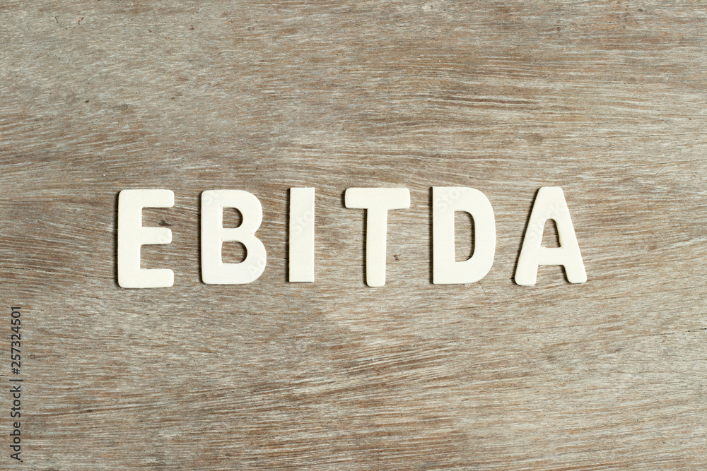 Alphabet letter in word EBITDA (abbreviation of earnings before interest, taxes, depreciation and amortization) on wood background
