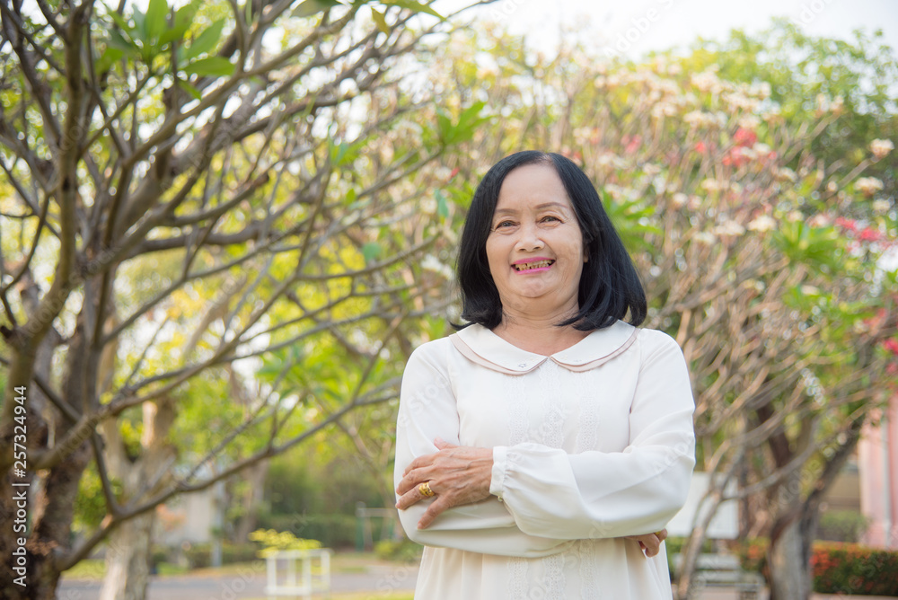 Beautiful asian senior woman standing and smiling in park Beautiful asian senior woman standing and smiling in park