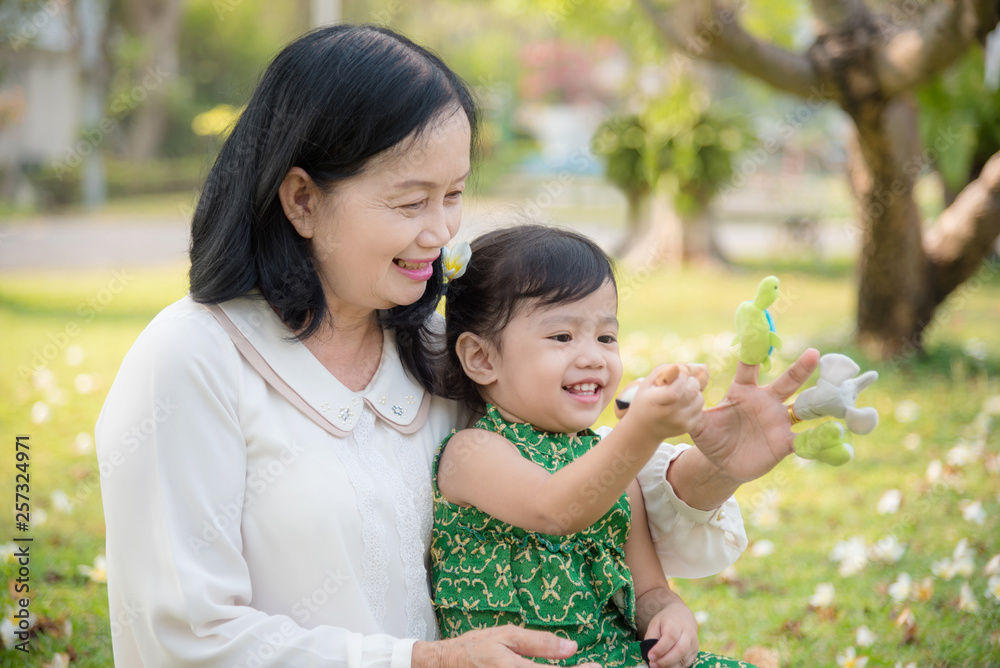 Asian Grandmother and granddaughter sitting and playing hand puppet together in the garden.Happy Asian family conception. Asian Grandmother and granddaughter sitting and playing hand puppet together in the garden.Happy Asian family conception.