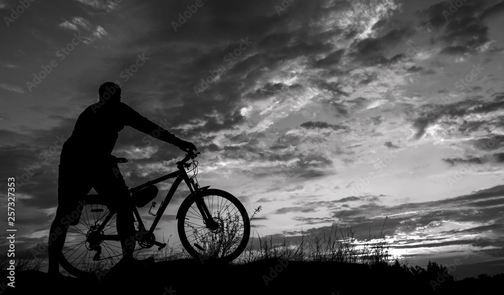 Fototapeta premium cyclist with a bicycle, in the background fiery sunset.