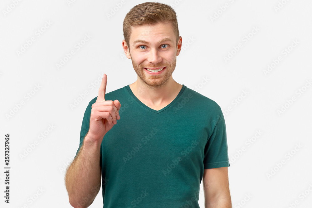 Stunned male points with fore finger upwards, he gets a good idea or good news about a successfully passed exam. Excited cheerful man remembers something nice, isolated on white background