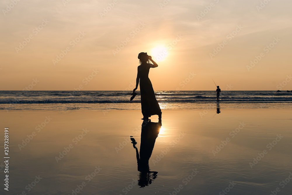 Contrast silhouette of a young slender woman against the background of a Sunny sunset, the sea and the sandy beach. 