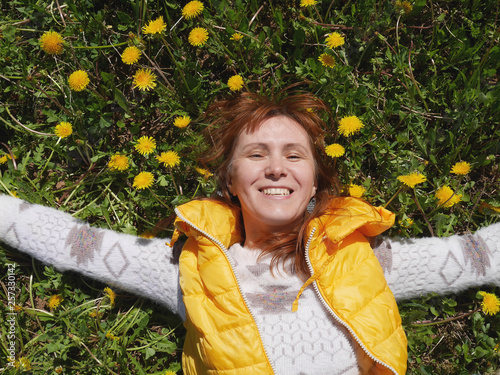 girl lying on the grass and his hands laid under his head. he smiles with his eyes closed. Dressed in a light sweater and yellow vest
