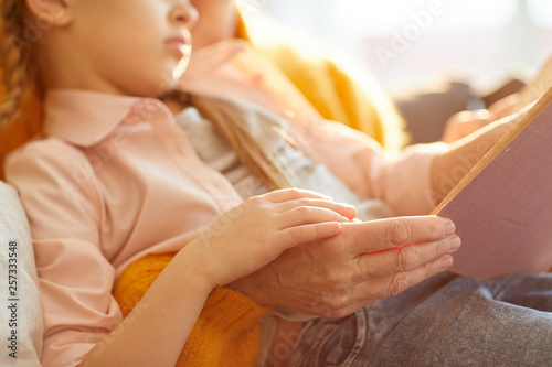 Closeup portrait of mature woman reading book to cute little girl in sunlight, copy space