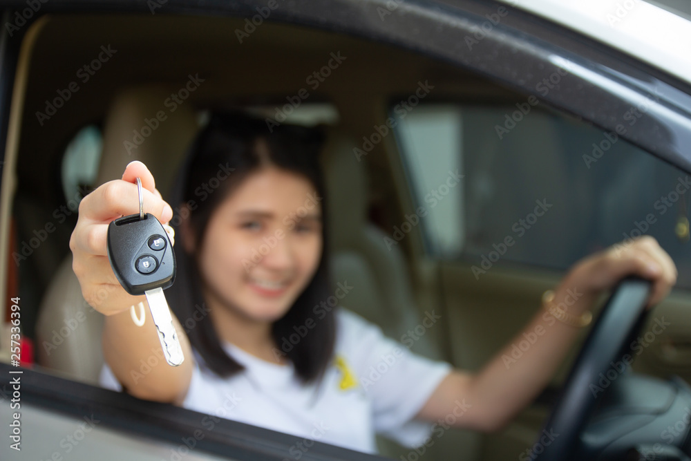 Asian car driver woman smiling showing new car key..Happy young girl owner taking car key from dealer in auto show room. Auto business, sale or rent car and people success driver license concept.