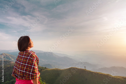 Rear view of a young woman standing on a mountain top peacefully gazing at low-lying morning clouds with copy space.